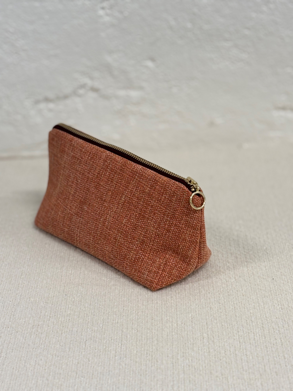 Praktisk og fin clutch i terra farge med fôr og glidelås i burgunder farge. Produsert av avkapp fra norske Wonderland Beds. Tekstilet har en coating på baksiden som gjør mappen stødig og gir den et eksklusivt preg.